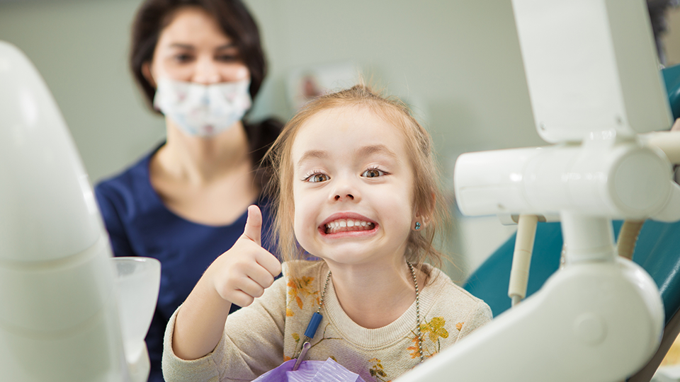 En nöjd flicka i tandläkarstolen visar tummen upp