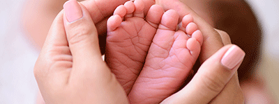 Spädbarnsfötter omfamnas av vuxna händer