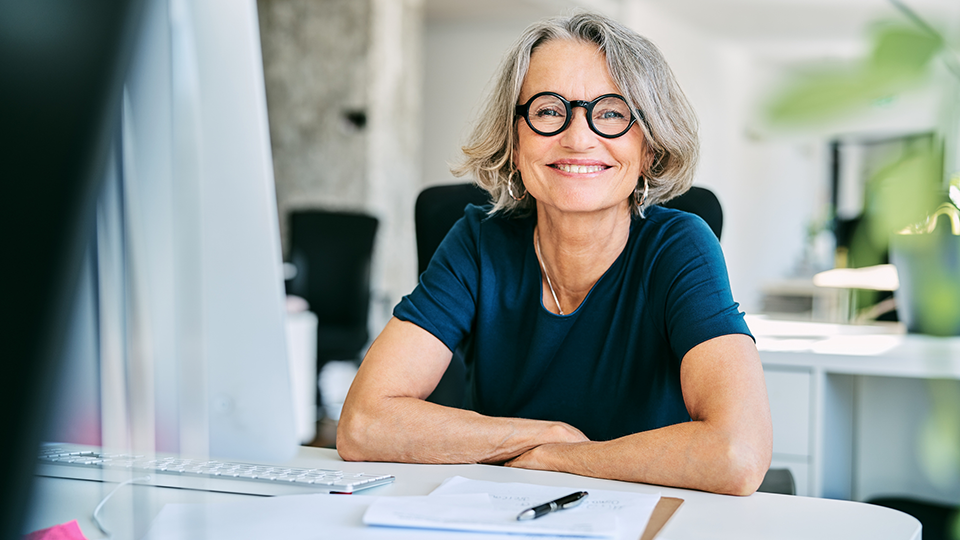 En leende kvinna i glasögon som sitte vid ett skrivbord